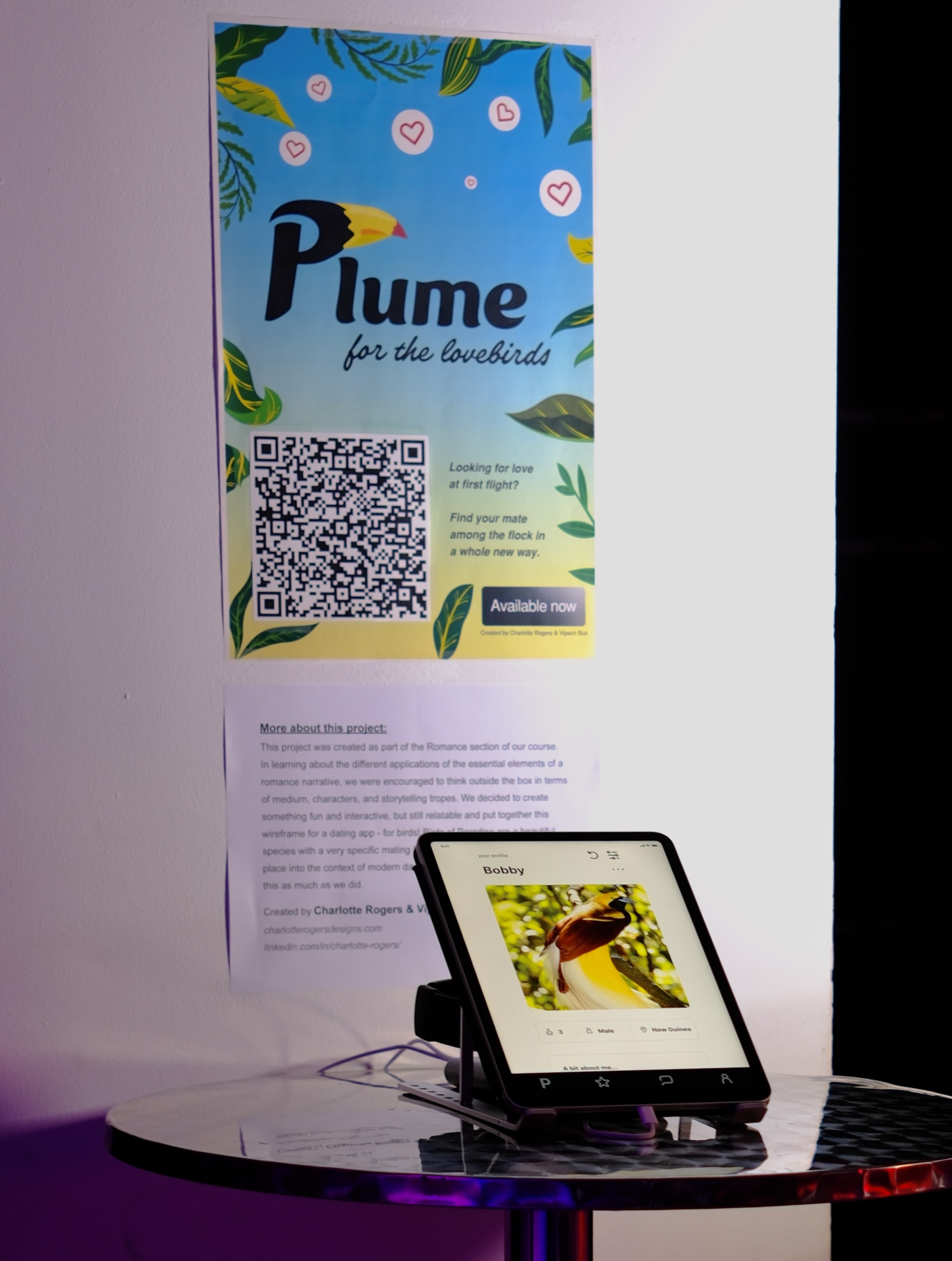 a poster with the project name, Plume, alongside project description page and iPad set up with Figma prototype on tall circular table under the room's purple light